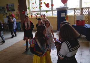 Grupa uczniów stoi na szkolnym korytarzu w trakcie przerwy. Mają na sobie kolorowe kostiumy postaci z bajek i baśni.